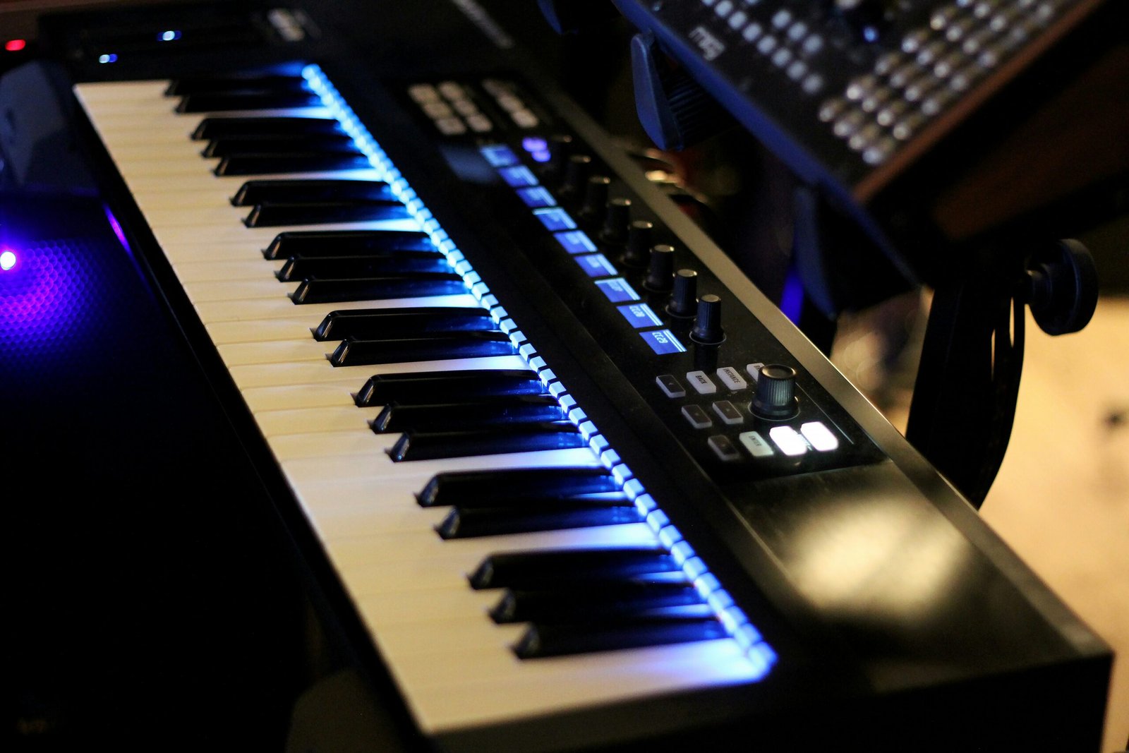 Close-up of a digital MIDI keyboard with illuminated control buttons and glowing blue backlight.