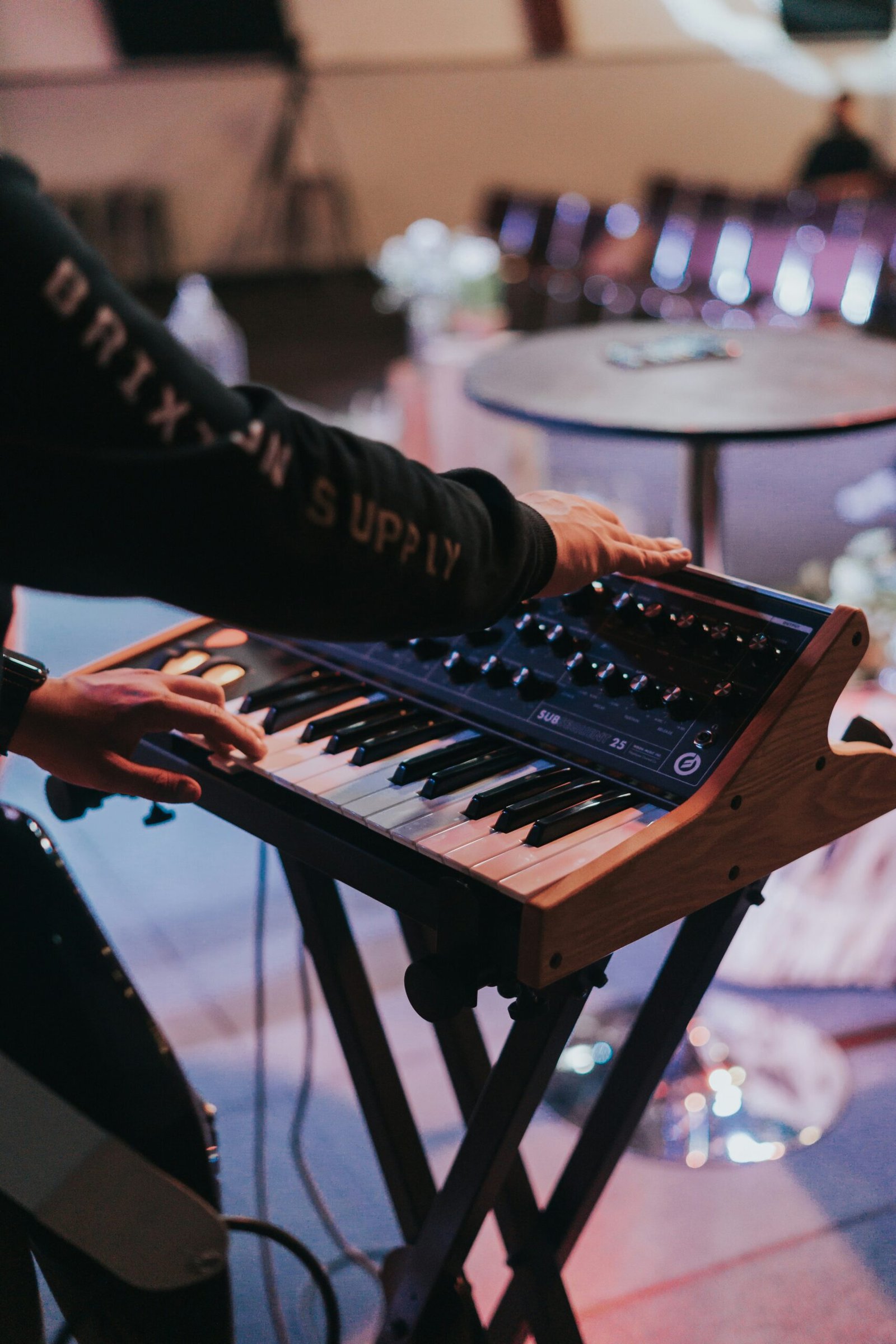 Musician playing a compact synthesizer on a stand during a live performance, adjusting sound knobs.
